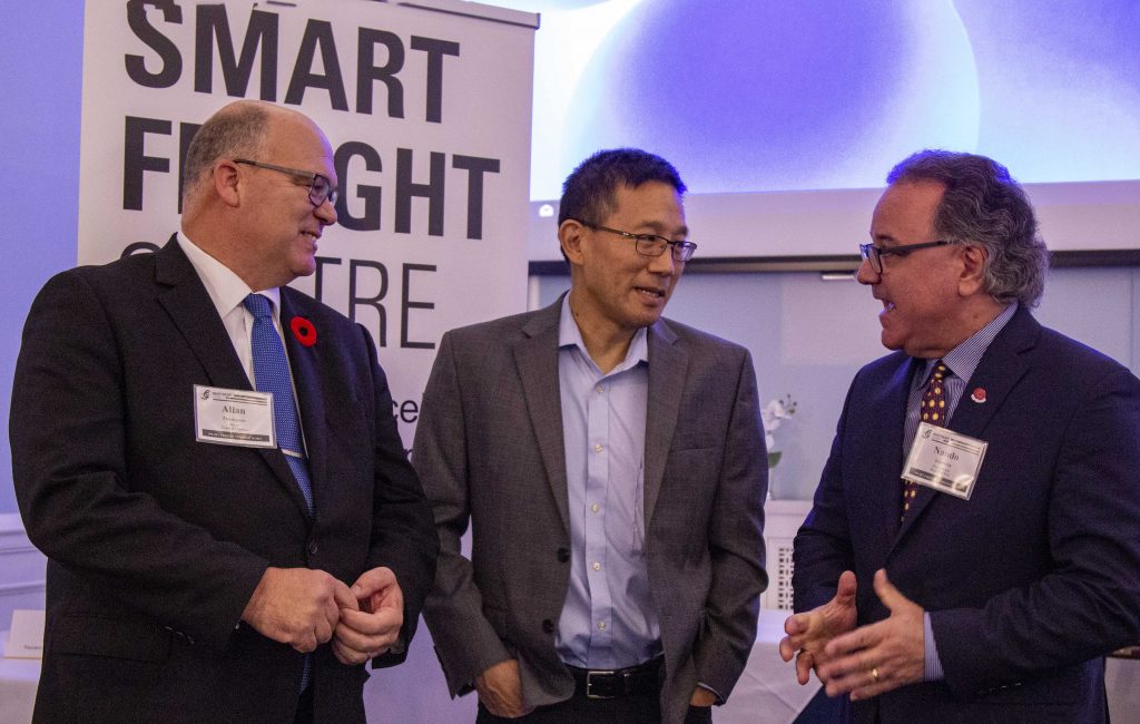 three standing chatting in front of Smart Freight Centre banner
