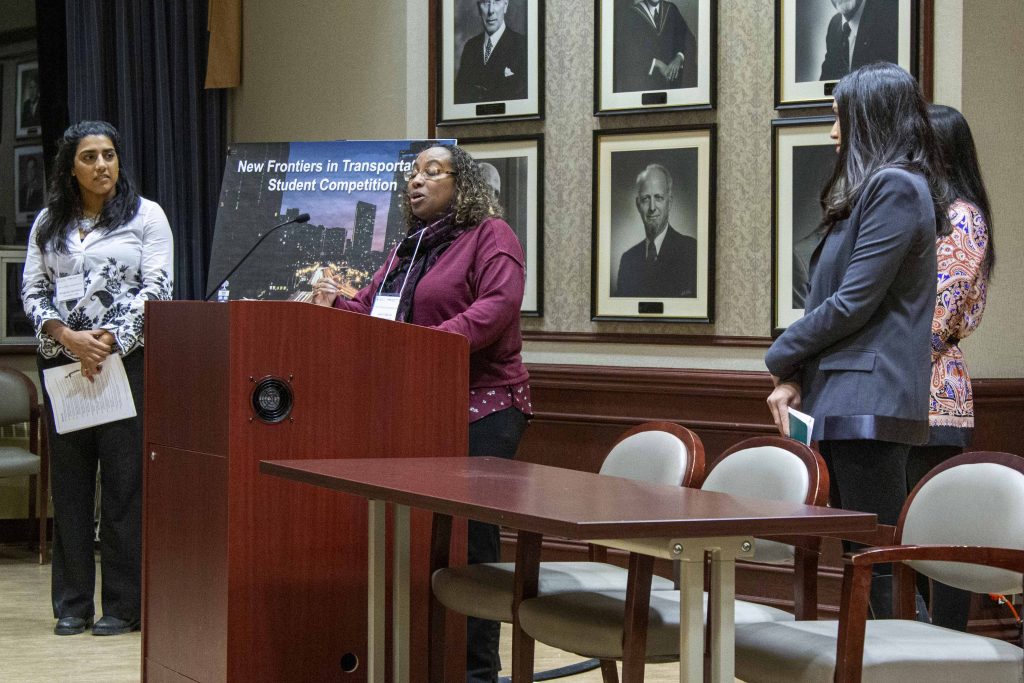 speaker at podium, three standing watching