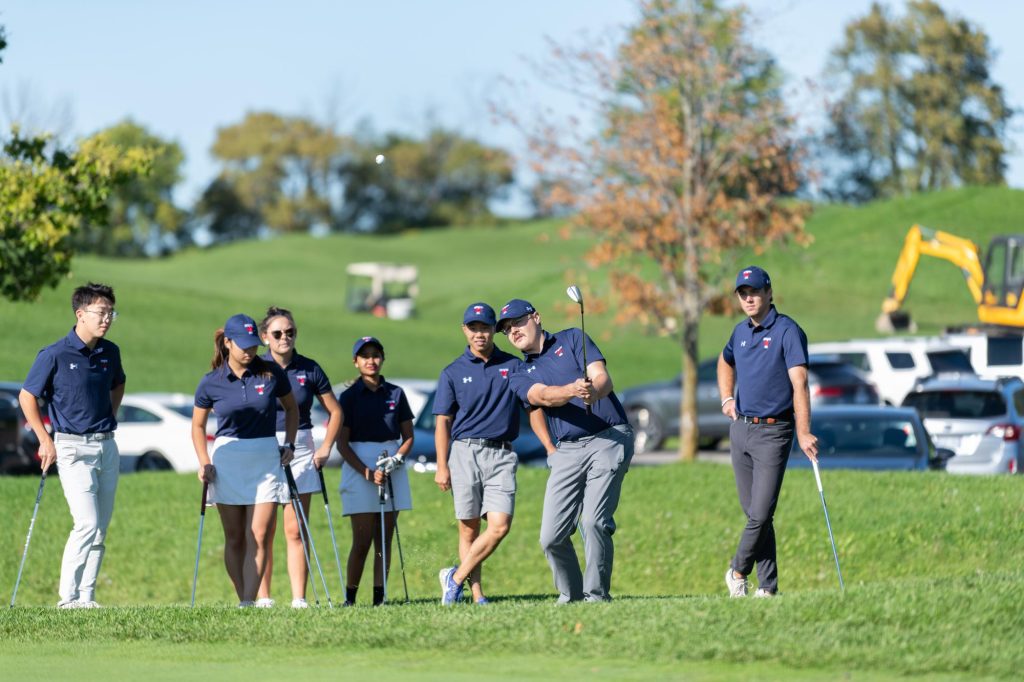 Varsity Blues golfing team surround Lavoie who swings
