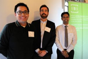 Three stand smiling at camera; green and white banner on right