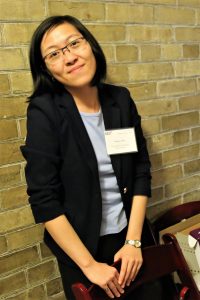 Standing leaning back against yellow brick wall holding back of chair