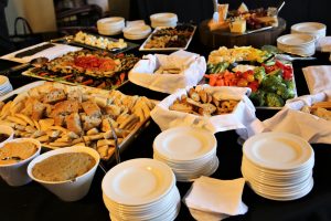 Piles of white plates and napkins, platters of food, dark tablecloth