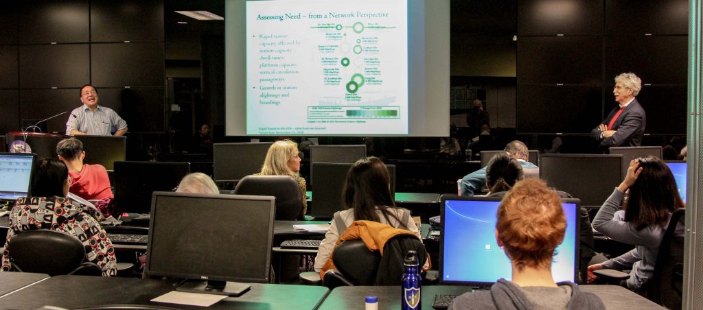 audience, speaker and moderator with screen at centre