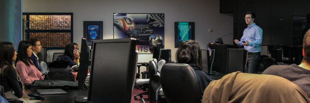 Speaker and audience in dimly-lit computer lab.